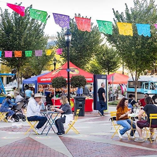 food-truck-dining Tables and banners in a downtown plaza with people eating and conversing.