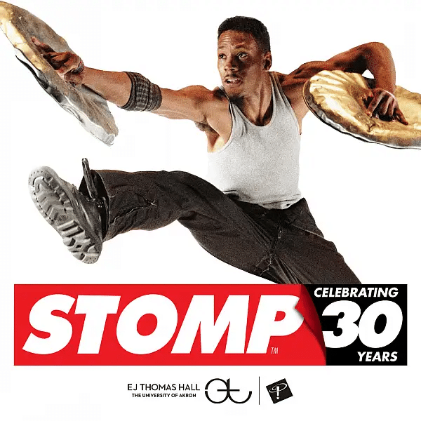 Photograph of one of the cast members of STOMP dancing / leaping, with 2 dented trash can lids in his hands.